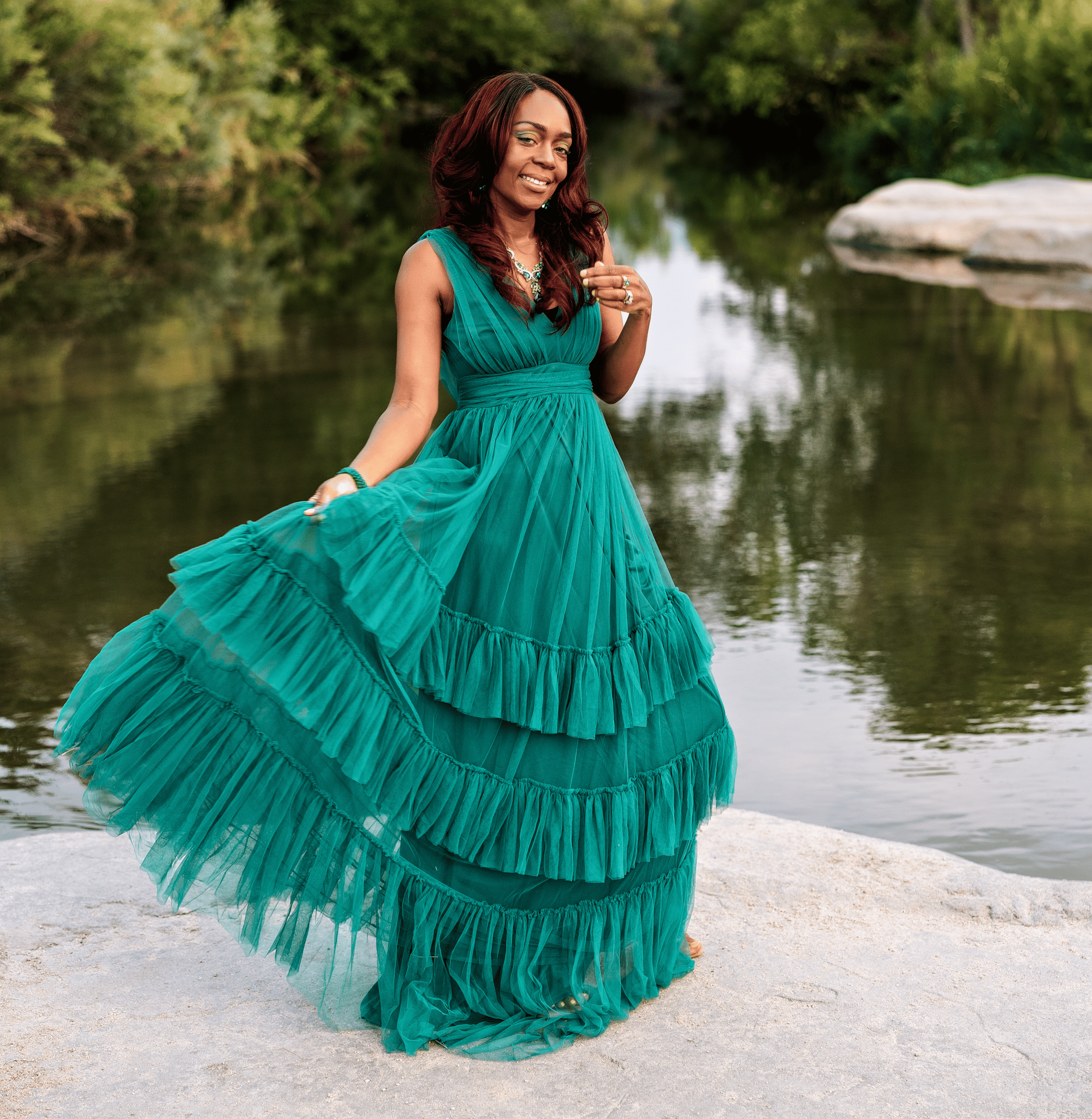 Lacricia Darling in a teal gown standing by a creek, celebrating her journey of healing